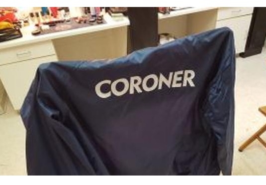 blue jacket with coroner in white letters on back draped on chair in office setting